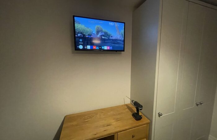 32-inch TV wall mounted high on a bedroom wall above a chest of drawers